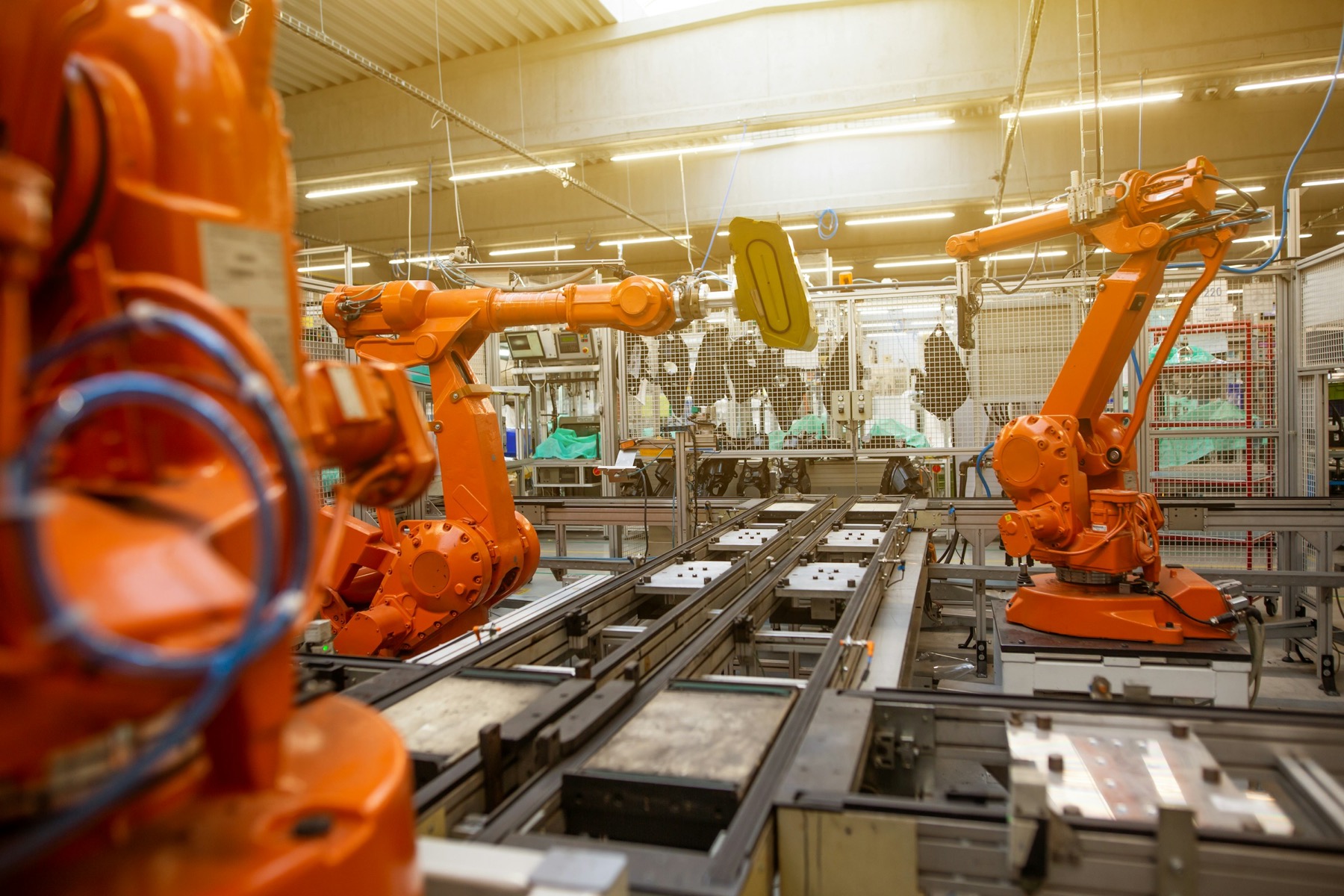 Orange industrial robots on a production line under factory skylights