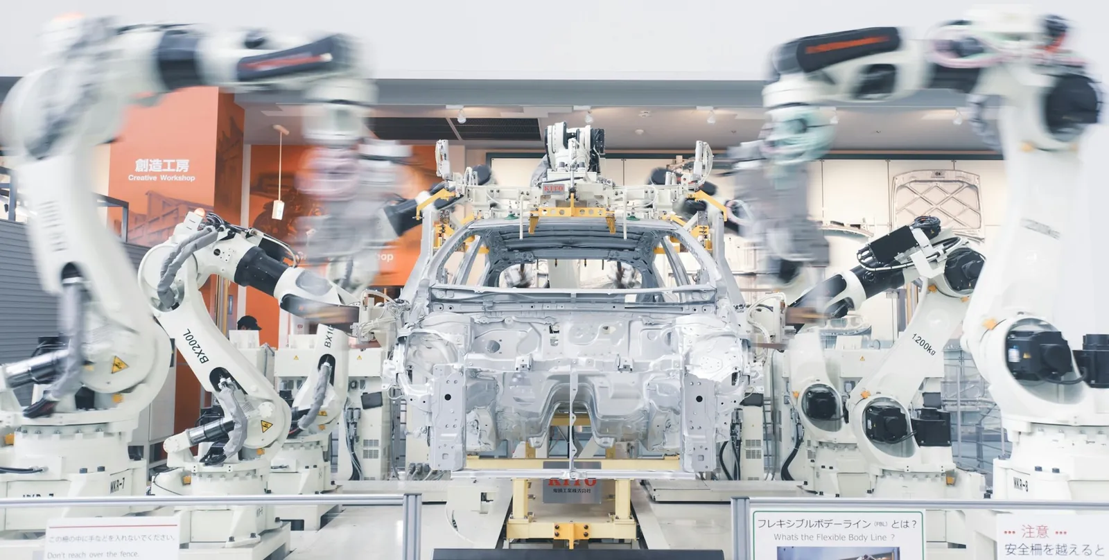 White industrial robots around a car body behind a safety fence