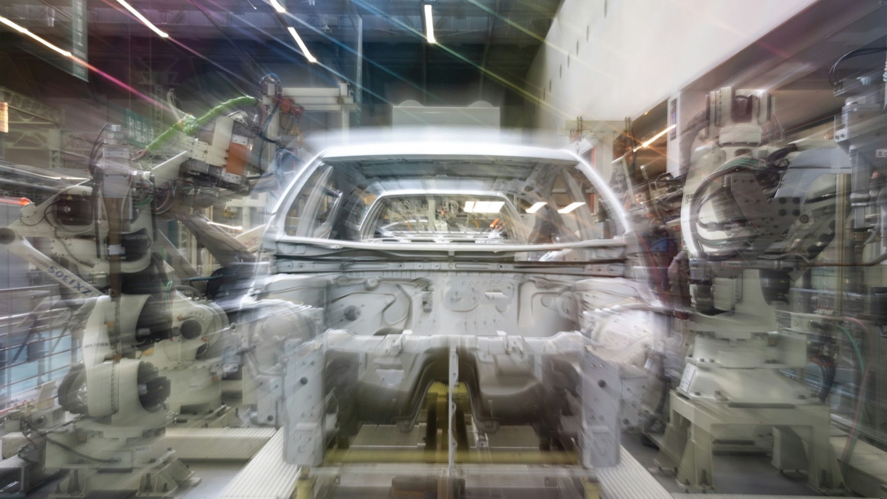 A car body moving through a robotic assembly line, motion blurred
